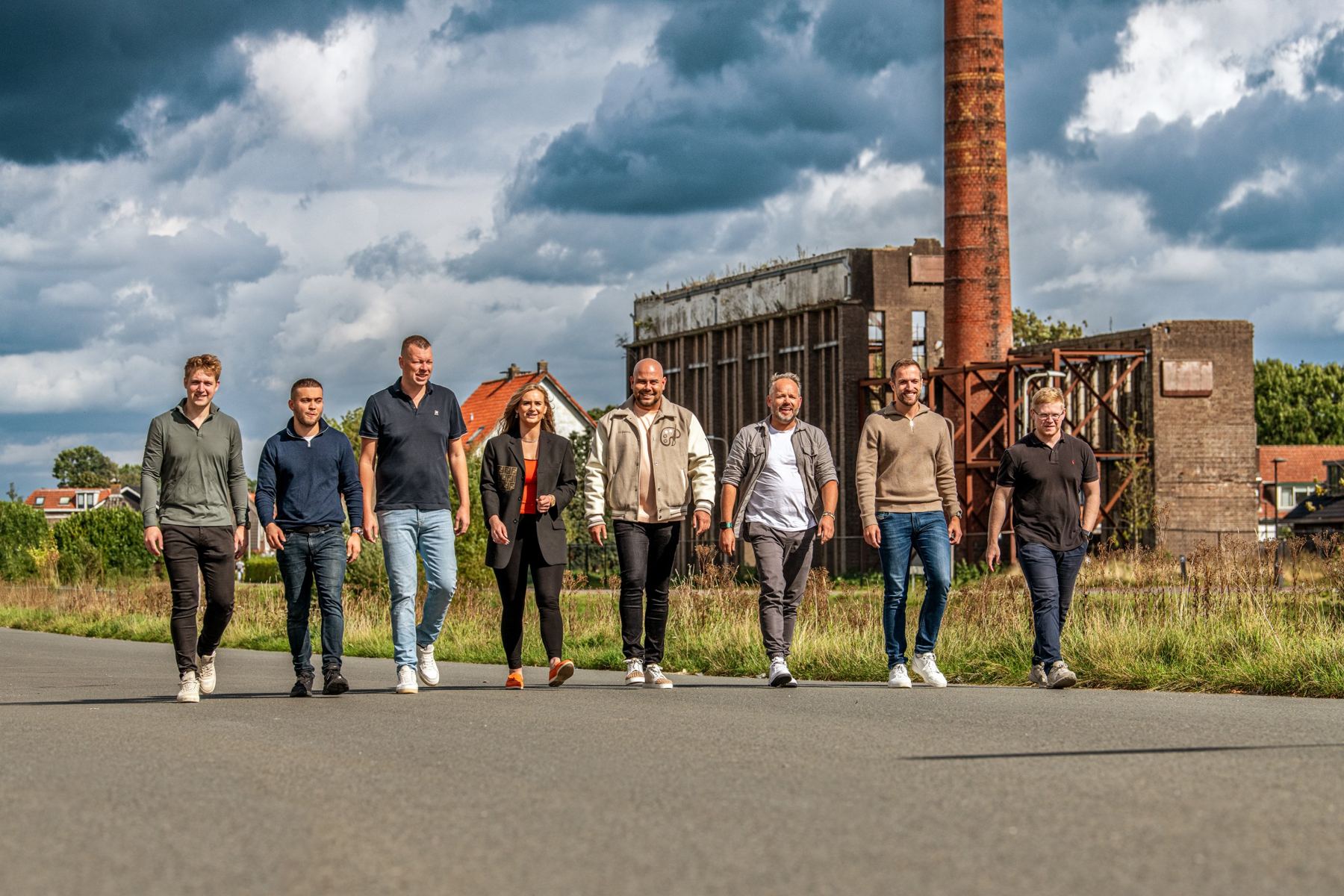 Het team van Level Up Club loopt samen over straat, met een oude fabrieksschoorsteen op de achtergrond